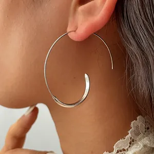 Close-up view of a large silver C-shaped geometric hoop earring worn by a model