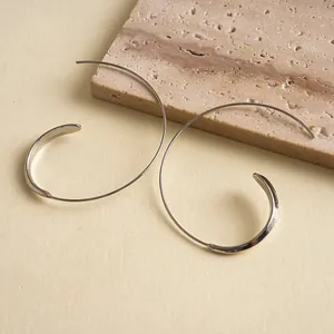 Close-up detail of minimalist silver-toned C-shaped geometric hoop earrings on stone