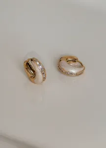 Detailaufnahme französischer Vintage-Goldohrringe mit schimmernden Zirkonen und weißem Email.