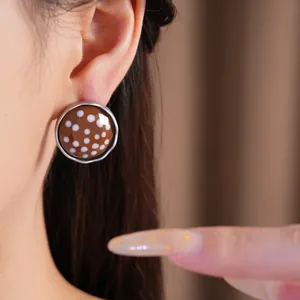 Close-up of minimalist brown and white polka dot round stud earrings being worn