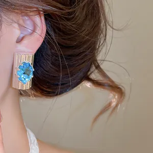 Elegante close-up van oceaanblauwe ovale zirkoon oorknopjes aan het oor van een model