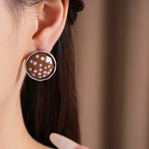Close-up detail of a stylish round glass stud earring with brown polka dots worn on an ear