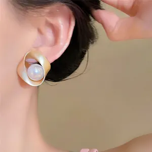 Eleganti orecchini a perno circolari intrecciati in oro opaco con perla centrale su modella