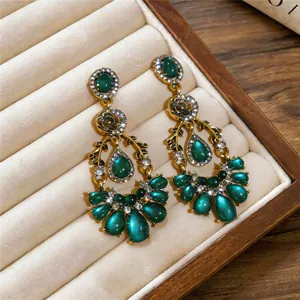Close-up view of vintage emerald green teardrop earrings with rhinestone flower accents