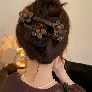 Close-up of a French style dark acrylic flower hair clip worn in a hair bun.