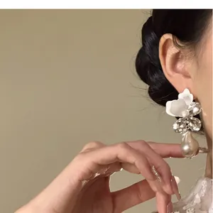 Detailopname van elegante stras bloemenoorbellen met een parelhanger aan het oor