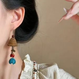 Close-up of ethnic wooden bell drop earring with teal floral tassel and red beads