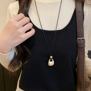 Detail shot of a minimalist matte gold pendant necklace with black cord on person