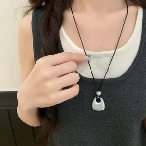 Detailed view of minimalist matte silver pendant necklace with black cord on model
