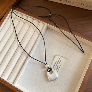 Detail view of a matte silver round pendant necklace on a cord in a wooden box