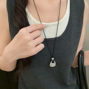 Close-up view of a minimalist silver pendant necklace with a black leather cord.