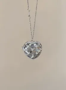 Detailopname van een zilveren hart medaillon ketting met strass rooster op beige achtergrond