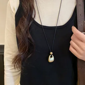 Close-up of a minimalist matte gold pendant necklace worn on stylish black knitwear