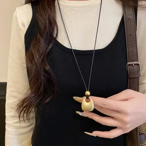 Detail of minimalist matte gold teardrop pendant on black cord sweater chain necklace