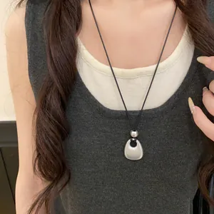 Detailed view of a matte silver geometric pendant necklace with black leather cord