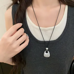 Close-up of a matte silver pendant necklace with a black leather cord worn on a model