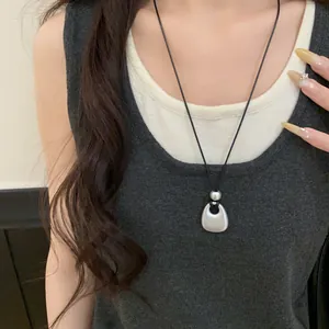Close-up of a model wearing a matte silver geometric pendant necklace with a black cord