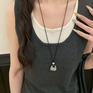 Close-up view of a minimalist silver U-shaped metal pendant on a black leather cord necklace