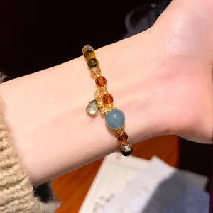 Close-up of retro crystal and tiger eye beaded bracelet with gold gourd charm on wrist.