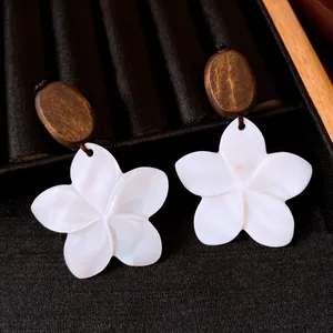 Artistic shell flower drop earrings with wooden studs displayed on black velvet cloth