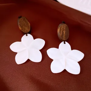 Detail view of white shell flower earrings with dark wooden bead accents and textures