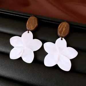 Close-up of elegant flower earrings with wooden tops and white shell-like floral pendants