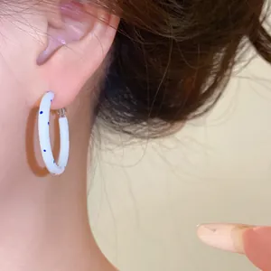 Detailansicht eines stilvollen weißen Creolen-Ohrrings mit blauen Punkten an einem Model