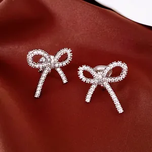 Detailed close-up of sparkling silver zircon bow knot ear clips on red silk fabric