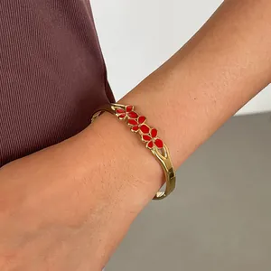 Détail d'un élégant bracelet jonc doré en acier avec de petites fleurs en émail rouge