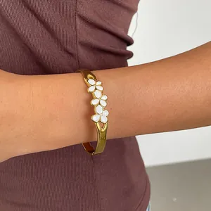 Gros plan d'un bracelet en acier inoxydable doré avec des fleurs en émail blanc au poignet