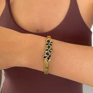 Détail d'un bracelet en acier doré avec des motifs floraux en émail noir porté au poignet