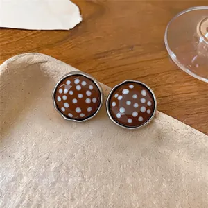 Detailansicht von braunen Vintage-Ohrsteckern mit Polka Dots auf einem strukturierten Tablett