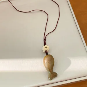 Dettaglio del ciondolo a forma di pesce in legno con perla a fiore su cordoncino rosso