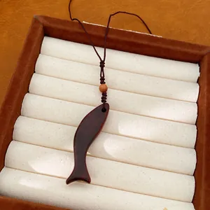 Dettaglio di un ciondolo in legno a forma di pesce fatto a mano su un cordoncino intrecciato.