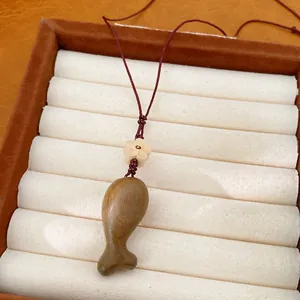 Primo piano di una collana con ciondolo a forma di pesce in legno su un vassoio.
