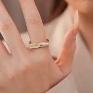 Nahaufnahme eines goldenen geometrischen Rings mit Zirkonia- und Muscheleinlagen.