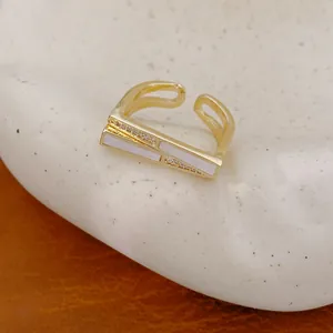 Detailansicht eines geometrischen vergoldeten Rings mit weißen Emaille-Einlagen