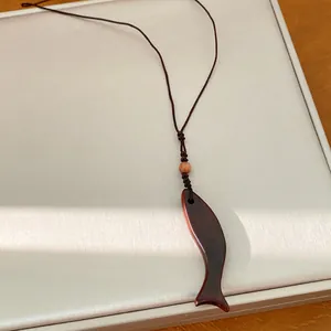 Dettaglio macro di una collana con ciondolo a forma di pesce in legno e cordino marrone