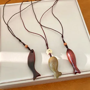 Primo piano di tre collane con pendenti a forma di pesce in legno su una scatola bianca testurizzata.