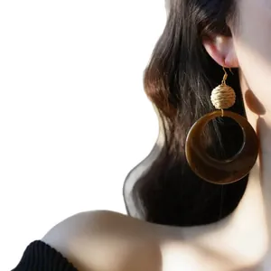 Élégantes boucles d'oreilles vintage en raphia et résine brune portées par un mannequin.
