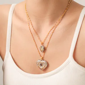 Détail des pendentifs en cœur bicolores sur plusieurs chaînes dorées superposées.