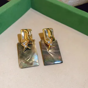 Gros plan de boucles d'oreilles dorées 18k avec étoiles en zircon et rectangles en nacre