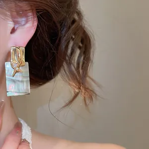 Gros plan élégant de boucles d'oreilles dorées avec étoile de mer et nacre carrée