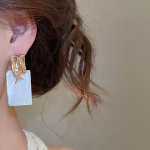 Vue détaillée d'une boucle d'oreille carrée en nacre avec une étoile en zircon doré