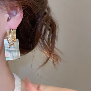 Vue rapprochée d'une boucle d'oreille rectangulaire en nacre avec étoile dorée et zircon.