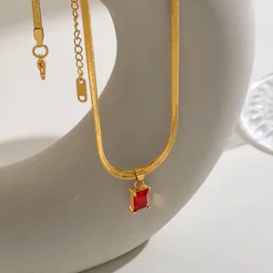 Detailopname van een gouden slangenketting met een rechthoekige rode edelsteen