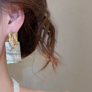 Détail de boucles d'oreilles carrées en nacre plaqué or 18k avec zircon sur un modèle
