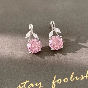 Close-up of pink rose-shaped zircon earrings with leaf details on gray background.