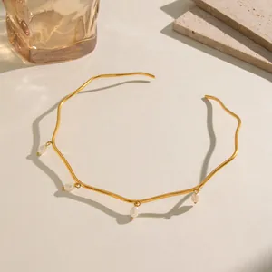 Dettaglio di un girocollo ondulato in acciaio dorato con eleganti ciondoli di perle