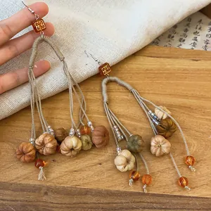 Detailed view of long tassel earrings featuring miniature handmade autumn pumpkin charms